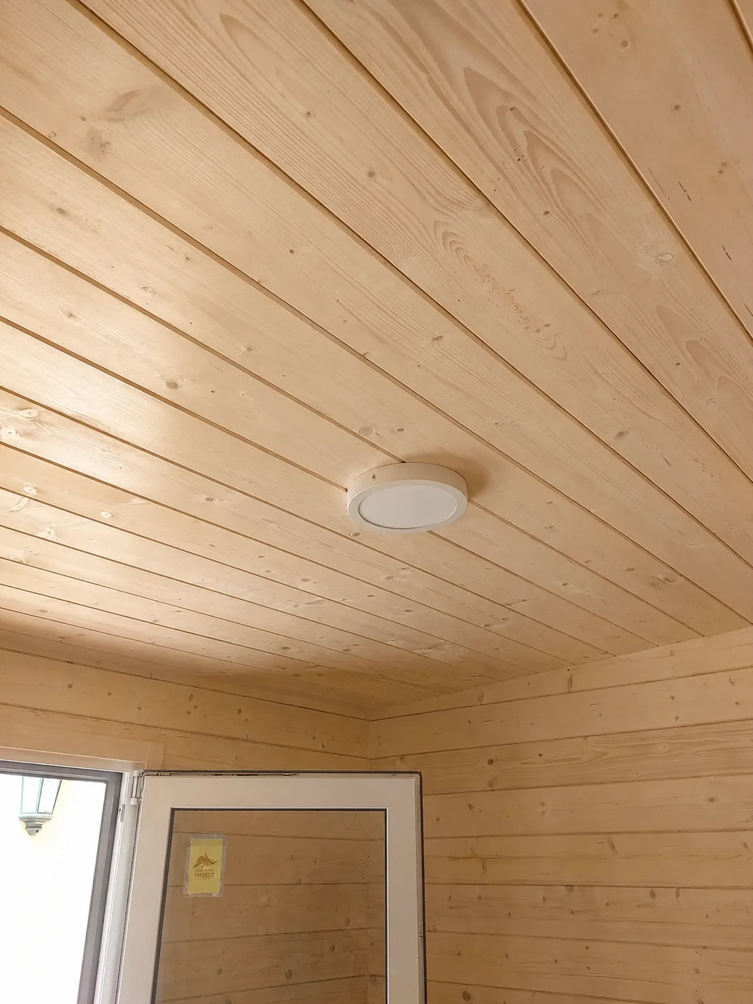 Techo interior forrado con friso de madera clara y plafón de luz
